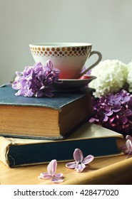 cup of tea on the stack of old books and spring lilac flowers