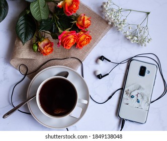 a Cup of tea on the table next to the phone, headphones and flowers.