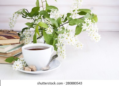 A cup of tea on a table with old books and flowers
