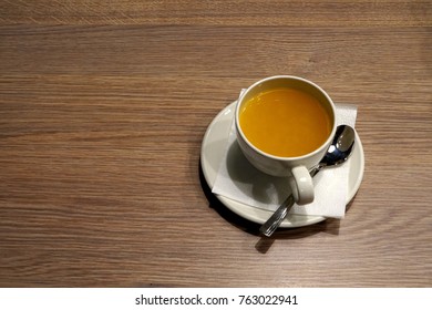 A cup of tea on the table.  View from above.  A cup on a saucer.  White ware.  Wooden countertop.  Silvery spoon on a napkin