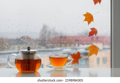 cup of  tea on windowsill with autumn leaves on window pane