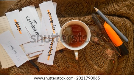 A cup of tea with some flash card of vocabularies in german. for german learners translated : on, actually, made up, salesman,
