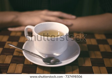 Cup of tea with spoon on the dish and woman's hands on the cafe table. Tea time.