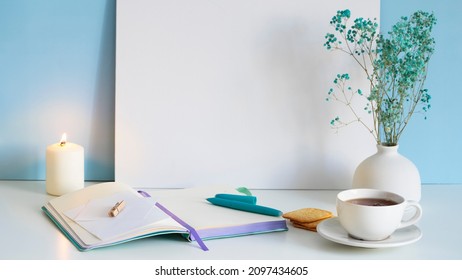 A cup of tea stands on a white table with a notebook, a pen, a burning candle. Preparation for writing the text.