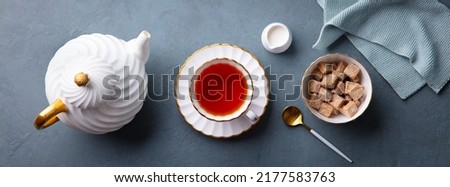 Cup of tea with teapot and sugar bowl. Grey background. Top view.