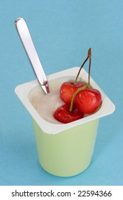 Cup of yogurt with fresh cherries on light blue background