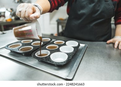 Cupcake baking. Professional pastry chef pouring chocolate batter into muffin paper moulds placed on muffin liners. High quality photo - Powered by Shutterstock