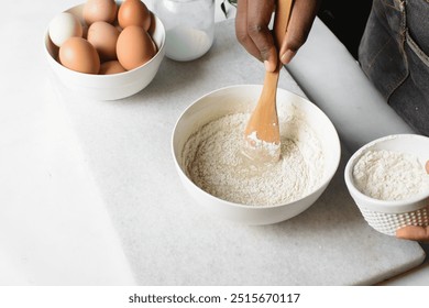 cupcake batter being mixed in a white mixing bowl, hand holding a wood spoon mixing vanilla cake batter - Powered by Shutterstock