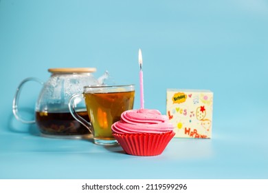 Cupcake With Birthday Candle Close Up And Teapod With Mug, Close Up On Blue Background.