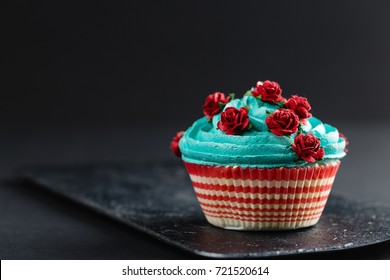 Cupcake with blue cream decorated with fake red roses on black background - Powered by Shutterstock