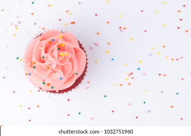 Cupcake Red Velvet With Blue And Pink Whipped Cream Decorated With Colorful Sprinkles On White Background. Top View.