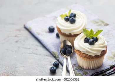 cupcakes with cream, blueberries and mint on a grey background