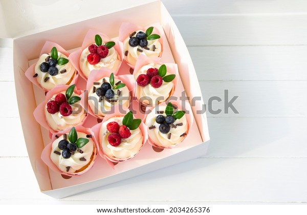 Cupcakes  decorated with raspberry\
and blueberries  in delivery paper box. Sweet food\
delivery