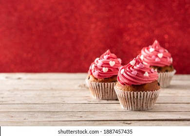 Cupcakes decorated with sugar hearts for Valentine's Day on wooden table and red background - Powered by Shutterstock