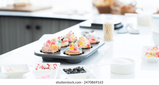 Cupcakes with pastel color butter cream, colorful jelly and chocolate flakes on baking tray in kitchen at home. Flour, sugar, eggs and decorating icing candy on table. Selective focus - Powered by Shutterstock