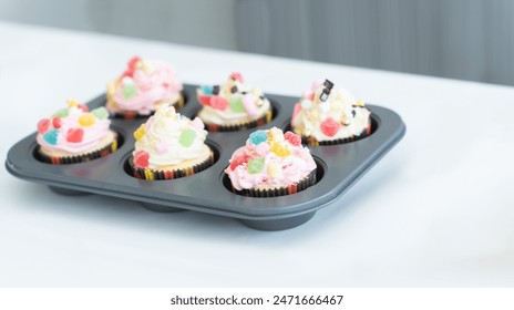 Cupcakes with pastel color butter cream, colorful jelly and chocolate flakes on baking tray on table in kitchen at home. Selective focus - Powered by Shutterstock
