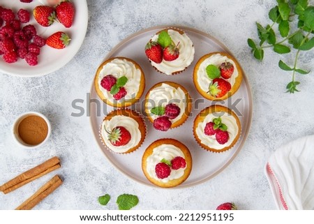 Cupcakes with raspberries and strawberries on a plate on a concrete background, top view