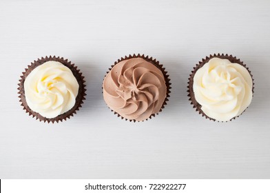 Cupcakes with whipped chocolate and vanila cream, on white wooden table. Picture for a menu or a confectionery catalog. Top view. - Powered by Shutterstock