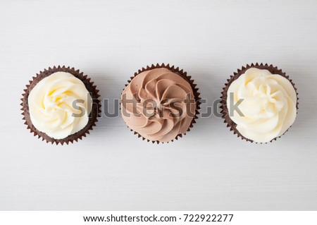 Cupcakes with whipped chocolate and vanila cream, on white wooden table. Picture for a menu or a confectionery catalog. Top view.