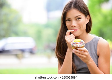 Cupcakes - woman eating cupcake in New York, Central Park, Manhattan. Business woman eating unhealthy food snack in lunch break smiling happy. Beautiful casual businesswoman in New York City, USA. - Powered by Shutterstock