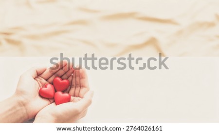 Cupped hands cradle three small red hearts on a clean white surface, symbolizing love and affection.