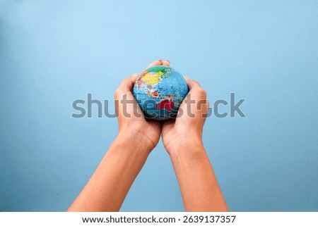Cupped Hands Holding Small Globe Against Blue Background