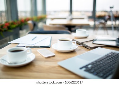 Cups with black coffee, gadgets and financial documents on table in cafe with nobody around - Shutterstock ID 1006223617