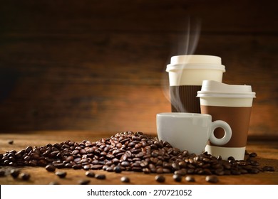 Cups of coffee with smoke and coffee beans on old wooden background