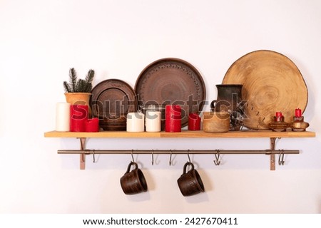 Cups hanging on metal cuisine railing on wall. Wooden shelf with various clay cookware and decoration in kitchen. Hanging storage. Organization of storage in the kitchen, open wall storage. Eco style