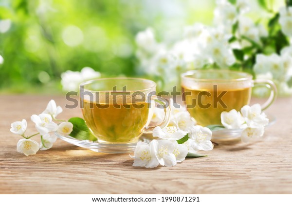 cups of jasmine tea and fresh jasmine flowers on a\
wooden table