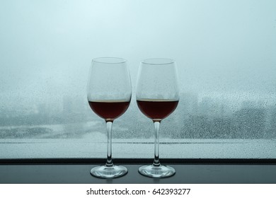 The cups of red wine on a rainy day window background.