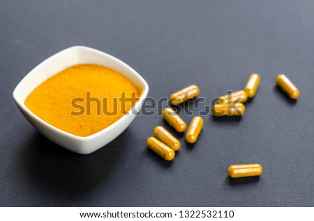 Curcuma or turmeric yellow powder and capsules on a dark background