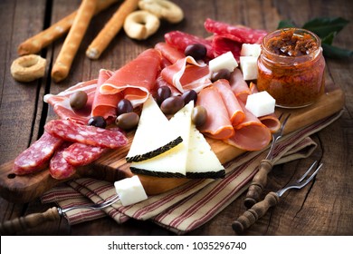 Cured meat and cheese platter of traditional Spanish tapas - chorizo, salsichon, jamon serrano, lomo and slices of goat cheese - served on wooden board with olives and bread sticks