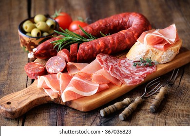 Cured meat platter of traditional Spanish tapas - chorizo, salsichon, jamon serrano, lomo - erved on wooden board with olives and bread