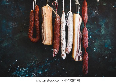 Cured meat and sausages hang with dry pepper from a rack at country house. Rustic dark style.
