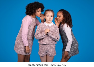 Curios international little girls in casual whispering secrets and gossip together, isolated on blue background, studio. Dream, communication, education at school, emotions children - Powered by Shutterstock