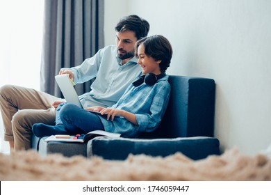 Curious Adult Man Pointing To The Screen While His Joyful Son Holding A Modern Laptop And Smiling