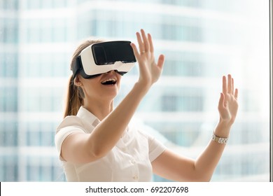 Curious amazed woman trying augmented reality glasses, feeling excited about VR headset simulation, exploring virtual life by gesturing hands to touch 3d world, having fun with goggles, head shot
