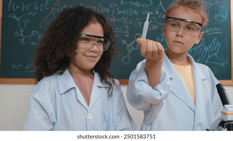 Curious american student standing at blackboard with chemical theory while doing experiment and discovery new sample. Attractive elementary smiling with confident while boy inspect solution. Pedagogy. - Powered by Shutterstock