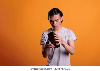 Curious Asian Man Opening Gift, Looking Inside Small Cardboard Box, Unboxing Present. Young Person Unpacking Surprise, Holding Delivery Parcel With Interested Facial Expression