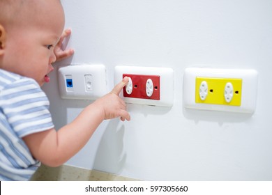 Curious Asian Toddler Baby Boy Child Play With Electric Plug. Try To Insert It Into Socket, Baby Hand Reach For Electrical Outlet Covered With Red Safety Plugs (child Safety Concept) - Selective Focus