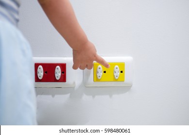 Curious Asian Toddler Child Play With Electric Plug.Try To Insert It Into Socket, Baby Hand Reach For Electrical Outlet Covered With Red Safety Plugs (child Safety Concept) - Selective Focus At Socket