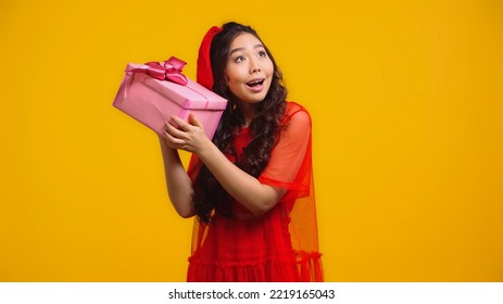 Curious Asian Woman Holding Wrapped Present Isolated On Yellow 