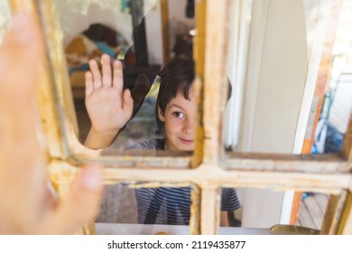 A Curious Boy Looks Out The Window, Portrait Of A Boy, Observation Through The Window, The Emotions Of A Child, Kid Looks Out Of The Window Of A House, Quarantine Self-isolation, Boy Waving.