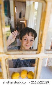 A Curious Boy Looks Out The Window, Portrait Of A Boy, Observation Through The Window, The Emotions Of A Child, Kid Looks Out Of The Window Of A House, Quarantine Self-isolation, Boy Waving.