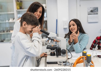 Curious boy using microscope with teacher assisting, learning science in school laboratory classroom