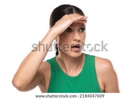 Curious brunette woman in green shirt looking far away with hand over head, trying to see something.