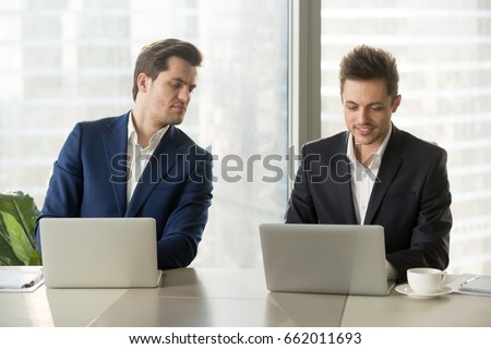 Curious businessman secretly looking at laptop screen of colleague, sneaking peek at other computer, stealing idea, copying private information on exam, nosy clerk spying on coworker at workplace
