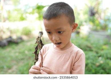 A curious child admires a stick in a lush garden, showcasing the wonder of nature and the joy of discovery in childhood exploration. - Powered by Shutterstock