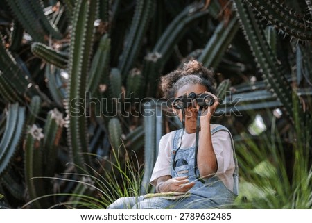 Curious child using binoculars while exploring a cactus collection in a tropical botanical garden. The image highlights eco education, wildlife observation, environmental literacy, biodiversity awareness, outdoor learning, and childhood curiosity inspired by nature.